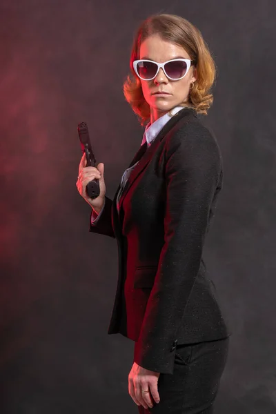 Una mujer mafiana con un arma en la mano. retrato sobre un fondo oscuro con luz roja . — Foto de Stock