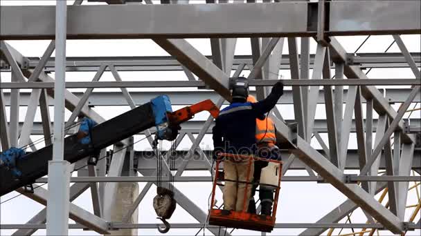 A welder working at height without insurance in a cradle lift in the construction of large shopping complex metal structures and concrete piles. — Stock Video