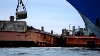 Suyla ilgilen. Bir yükleyici bir mavnadan bir gemiye kömür yükler. rapor çekimi.