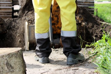 İnşaat işçisi yol kenarını genişletirken kazıcıyı yönetiyor..
