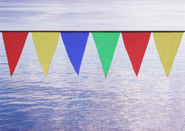 Banderas triangulares multicolores que cuelgan en el cielo al aire libre sobre el fondo de agua azul . — Foto de Stock