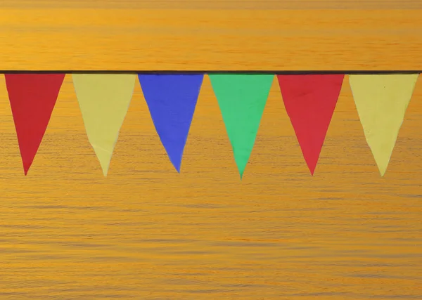 Banderas triangulares multicolores que cuelgan en el cielo al aire libre sobre el fondo de agua dorada . — Foto de Stock