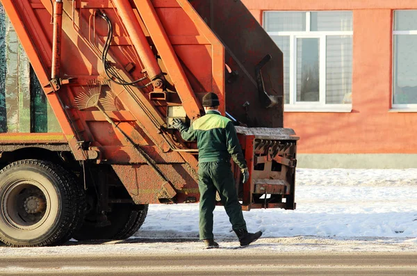 Werknemer permanent naast een ongewenste auto na het laden van huisvuil tank. — Stockfoto