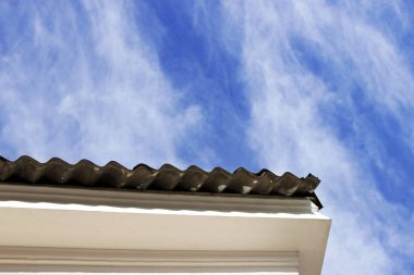 Evin tepe örtüsü, dalgalı çatı malzemesi, yazın bulutlu mavi gökyüzü.