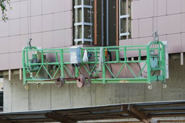 Yeşil cephede çalışmak. İki askıya alınmış beşik. İşçiler olmadan yeni inşa edilmiş yüksek binalarda.