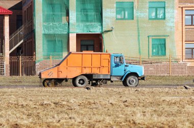 Turuncu şehir süpürgesi baharda yuvarlak bir fırçayla toprağı temizliyor..