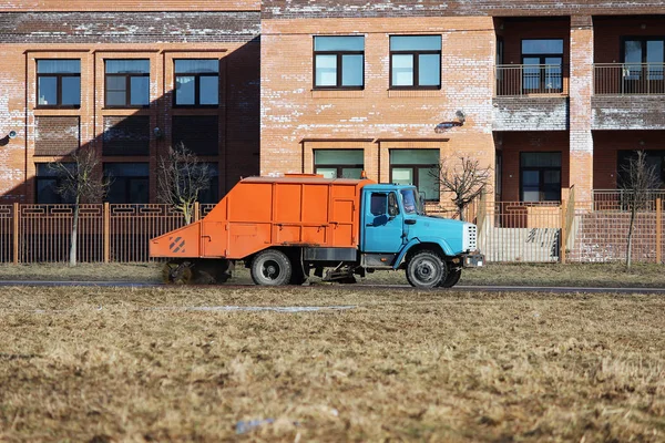 Oranje stedelijke veegmachine reinigt weg van vuil met een ronde borstel in het voorjaar. — Stockfoto