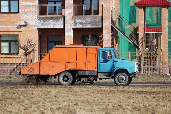 Barredora urbana naranja limpia carretera de la suciedad con un cepillo redondo en la primavera. —  Fotos de Stock