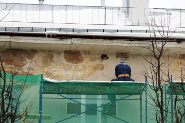 Koruyucu gözlüklü ve solunum cihazlı işçi, restorasyon ve alçıdan önce duvarı açı öğütücüyle işliyor..