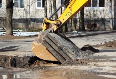Yer altındaki kazaları elerken yol yüzeyini açmak. Özel eklentisi olan bir traktör ve kovası olan bir kazıcı.