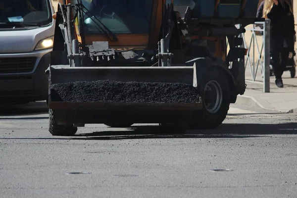 Mini excavator transports in the scoop asphalt crumbs to repair road pits in the city of st. Petersburg.