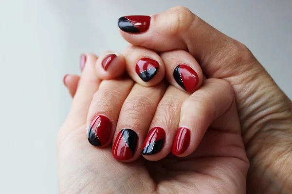 beauty delicate red black manicure with gel varnish on a white wall background