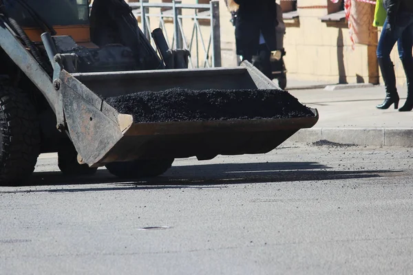 Mini excavator transports in the scoop asphalt crumbs to repair road pits in the city of st. Petersburg.