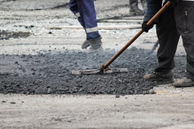 İşçi, asfalt kırıntılarını kaldırıma asfalt döşemeden önce kaldırım taşıyla düzleştiriyor.
