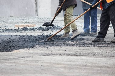 İşçi, asfalt kırıntılarını kaldırıma asfalt döşemeden önce kaldırım taşıyla düzleştiriyor.