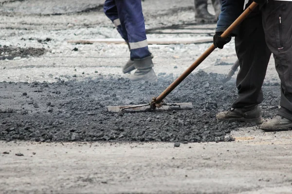 The worker is leveling the crumb of asphalt in the pit with a drag-roller before the paving with a road mini building roller