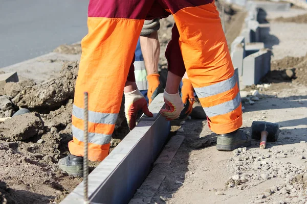 Reparation av trottoaren. Professionell arbetande frimurare i overaller låg trottoarkanter innan du lägger sten stenbeläggningen plattor. — Stockfoto