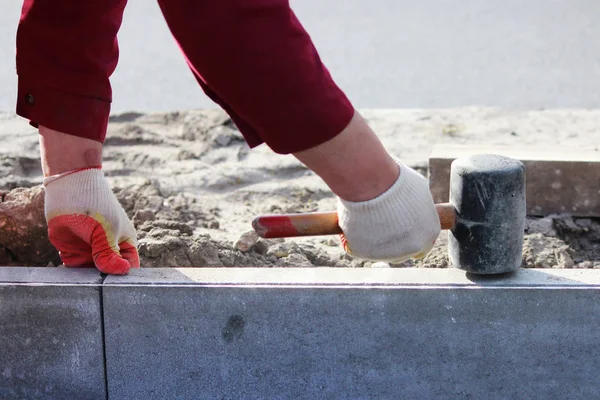 Repair of the sidewalk. Professional working masons in overalls lay curbs before laying stone paving slabs.