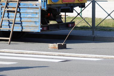 İşçiler, zebra şeritli yaya geçidine beyaz boya ile bir yol işareti koyuyor ve trafik ışığının yanındaki asfalta yansıtıcı bir toz serpiştiriyor..