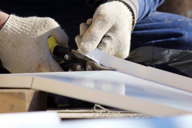 İşçi şehrin yenilenmiş binasındaki pencereleri kapatıyor, yamaç için metal levhayı makasla kesiyor.