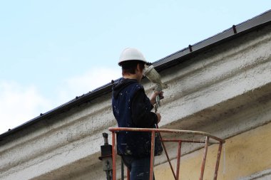 Genç bir işçi ressam şehir Demiryolu İstasyonu yükseklikte bina bir Asansör yardımıyla duvarına beyaz çizgi boyalar