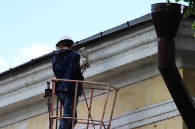 Genç bir işçi ressam şehir Demiryolu İstasyonu yükseklikte bina bir Asansör yardımıyla duvarına beyaz çizgi boyalar