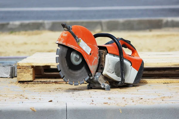 Una sierra circular para aserrar una placa de bordillo se encuentra cerca de una plataforma de madera cuando se construye un estacionamiento para autobuses turísticos . — Foto de Stock