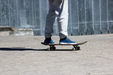 Kaykaycı beyaz pantolonlu kaykaycı şehir meydanında fıskiyelerin yanında kayıyor.