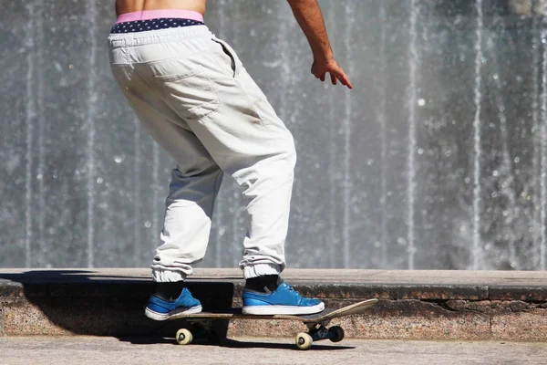 在靠近喷泉的城市广场上 穿着白色长裤滑冰的滑板手 — 图库照片