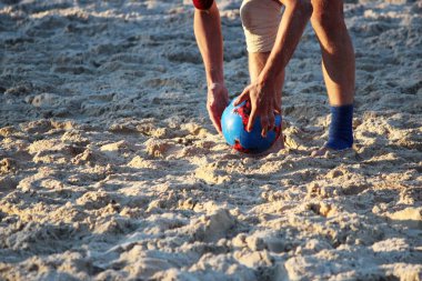 Gençler yazın kum platformunda futbol oynarlar.