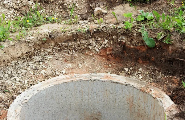 Bene per l'estrazione dell'acqua. La costruzione di un pozzo villaggio per l'estrazione di acqua con l'aiuto di diversi anelli di cemento posato in una fossa di terra — Foto Stock