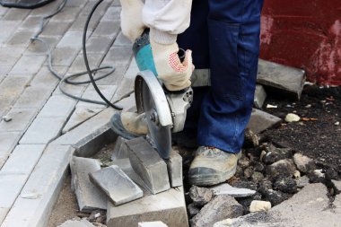 İşçi bir duvar ustası kaldırımı tamir ederken dairesel testere ile kaldırım kenarını kesiyor..