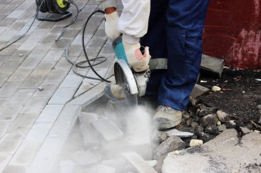 İşçi bir duvar ustası kaldırımı tamir ederken dairesel testere ile kaldırım kenarını kesiyor..