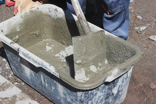 İşçi yol kenarındaki trafik ışıklarının altındaki desteğin temeli için banyo ve kürek yardımıyla çimento yoğurur..