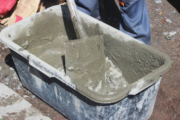İşçi yol kenarındaki trafik ışıklarının altındaki desteğin temeli için banyo ve kürek yardımıyla çimento yoğurur..