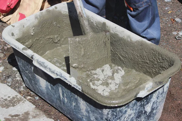 İşçi yol kenarındaki trafik ışıklarının altındaki desteğin temeli için banyo ve kürek yardımıyla çimento yoğurur..