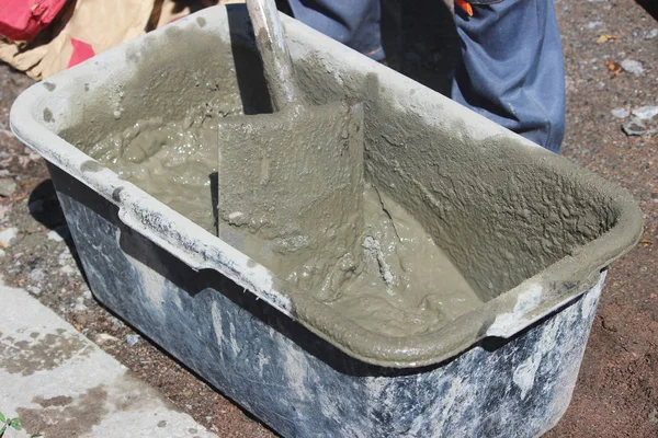 İşçi yol kenarındaki trafik ışıklarının altındaki desteğin temeli için banyo ve kürek yardımıyla çimento yoğurur..
