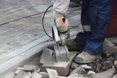 İşçi bir duvar ustası kaldırımı tamir ederken dairesel testere ile kaldırım kenarını kesiyor..
