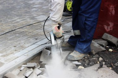 İşçi bir duvar ustası kaldırımı tamir ederken dairesel testere ile kaldırım kenarını kesiyor..