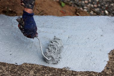 Erkek bir ressam, bir yeraltı yaya geçidinin yanında boya silindirli gri bir boyayla beton bir yamaç boyuyor..