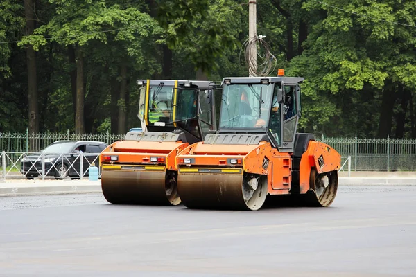 İki turuncu sıkıştırıcı gelecekte turist otobüsleri için otoparkta asfalt yapıyor. Gatchina