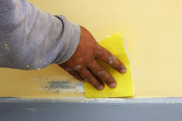 Work plasterer processes the wall of the house with sandpaper. Elimination of poor-quality work before re-coating with paint