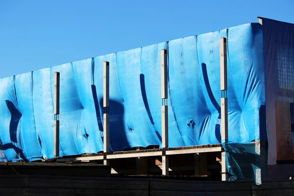 Centro comercial edificio abandonado sin vigilancia saqueados por los vándalos están cubiertos con una red de construcción azul antes de las vacaciones en la ciudad en un cielo azul de fondo — Foto de Stock
