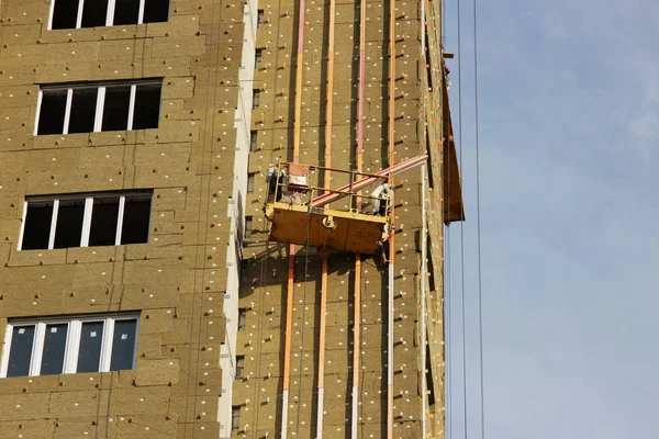 Arbeiter in gelber Hängewiege montiert Umweltplatten zur Isolierung an einem neu errichteten Hochhaus — Stockfoto