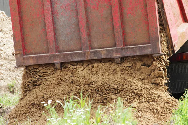 Camión de construcción descarga arena en el sitio de reparación donde la colocación de la tubería con agua. Toldo publicitario amarillo vacío en la cabina — Foto de Stock