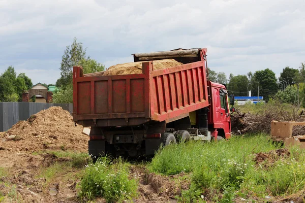 Construction truck unloads sand at the site of repair where laying the pipeline with water. Yellow empty advertising awning on the cab