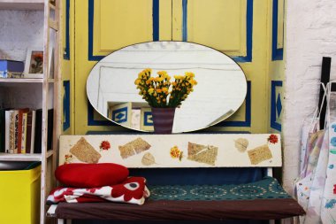 Yaratıcı alan. Oval bir ayna, kitaplar, sarı çiçekler karanfil bir vazo ve bir kanepe yastıkları arka planı mavi çizgili sarı bir kapı ile rahat ev iç.