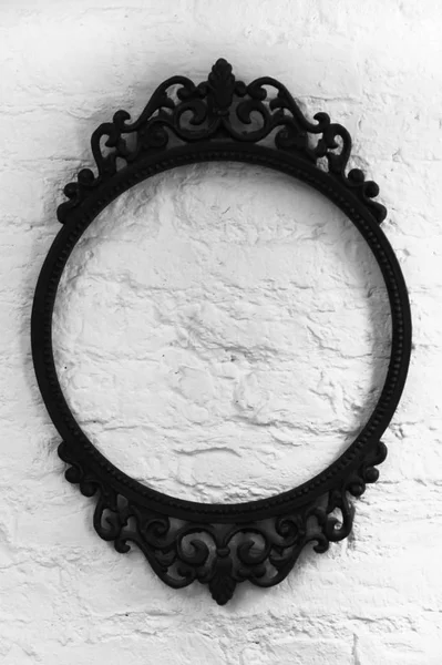 An oval patterned empty metal frame on a white wall background. black and white photo — Stock Photo, Image