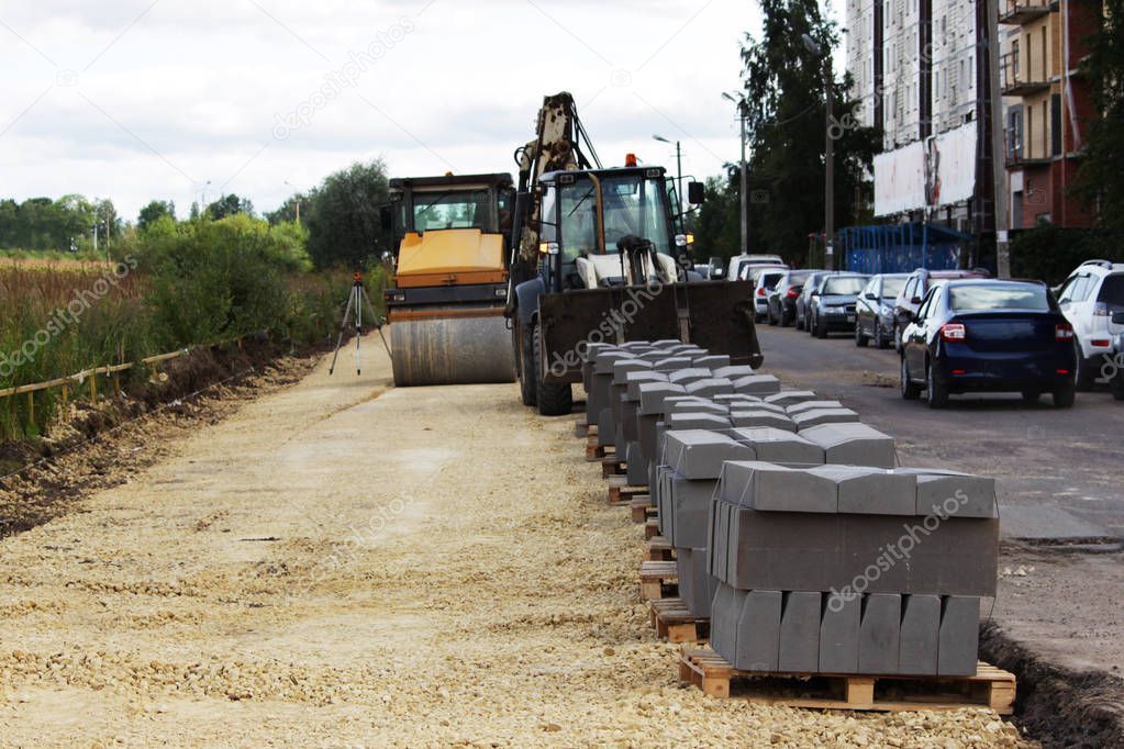 preparation for the repair of the site before the laying of paving slabs. The roller compacts the surface, the loader unloads the paving slab on pallets.