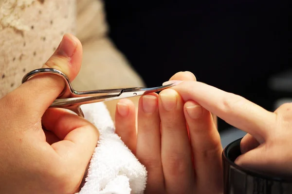 A student at the training courses of a manicure prepares the hand of a lady client with a manicure scissors for cuticles before applying shellac.
